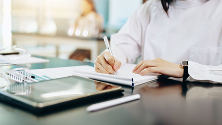 Woman, hands and writing with notebook for research, study or medical discovery at laboratory. Closeup, female person or scientist taking notes in exam, test or clinic trial for lab results on deskの写真素材