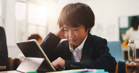 School, tablet and sad child with stress, leaning and development in classroom. Assessment, anxiety and test with virtual language course, research and japanese student app for knowledge on websiteの写真素材