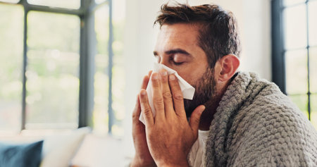 Sick, man and sneezing with blanket in home for flu symptoms, fever and respiratory disease on sofa....