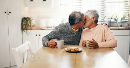Hug, kiss and senior couple with coffee, home and bonding with beverage in kitchen and elderly people. Happy, old man and mature woman with tea in house, comfortable and embrace for love in morningの写真素材