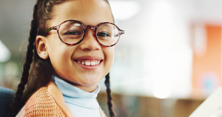 Portrait, kid and girl in library, glasses and smile with confidence, optometry and education. Face, student and child development with eyewear, clear vision and pride with knowledge or future growthの写真素材