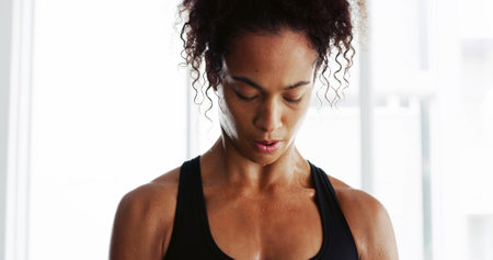 Sweat, fitness and woman tired in gym for intense training, exercise and workout in morning. Sports, athlete and person with fatigue on break, resting and breathe for wellness, health and challengeの写真素材