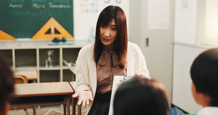 Teacher, children and English lesson in classroom for language development, group project and growth. Japanese students, reading together or studying with educator for support, knowledge or helpの写真素材