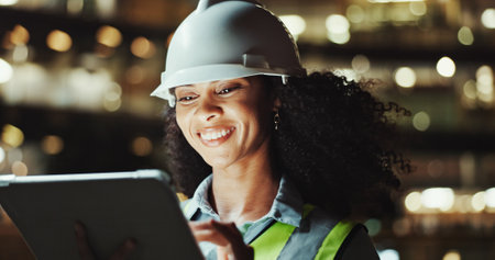 Tablet, architect and happy woman outdoor for development, construction or planning at night. Technology, building or African engineer in city for maintenance, safety inspection or project with bokehの写真素材
