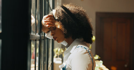 African woman, window and anxiety in home with headache, mistake or regret with reflection for decision. Person, sad and thinking for perspective, loss or grief with mental health in morning at houseの写真素材