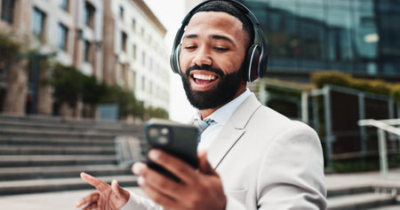 Business, man and phone with headphones in city for music playlist, morning commute or streaming audio. Professional, dancing or happy outdoor for sound subscription, work break or listening to radioの写真素材