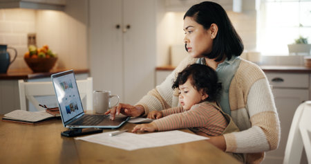 Multitasking, child and mom with laptop, remote work and editing article in kitchen with baby or online. Serious, writer and woman with toddler in house, screen and person with project for blogの写真素材