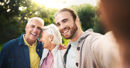 Selfie, park and senior parents with son for bonding, relationship and relax together. Portrait, happy family and elderly dad, mom and man embrace outdoors for love, affection and social media postの写真素材