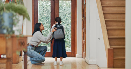 Mother, girl and backpack for school at front door with motivation, care and love in morning at house. Mom, child and kindness with support for learning, education and scholarship at family homeの写真素材