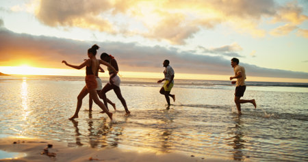Sunset, running and friends at beach by water for holiday, vacation and summer trip on tropical island. Group, ocean and people race at sea with energy for freedom, travel and excited for adventureの写真素材