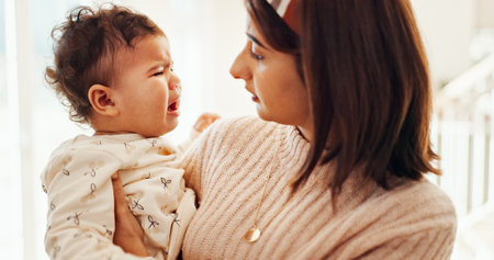 Mom, baby and crying in home with comfort, care and love with connection in morning at family house. Infant, mother and daughter for kindness with embrace, bonding and support with voice at apartmentの写真素材