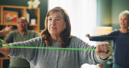 Senior woman, resistance band and exercise by group with breathing in workout, health or transformation in retirement. Person, equipment and friends for training, muscle or stretching at fitness clubの写真素材