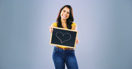 Portrait, smile and woman with heart on black board of self love, spread kindness and celebrate moments. Person, sign and space for advertising romance, passion and happiness in studio backgroundの写真素材