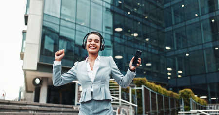 Business, headphones and woman in city, celebration and smile with audio, listening to music and success. Happy person, dance and consultant with cellphone, promotion and headset with sound or radioの写真素材