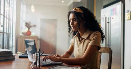 Girl, student and laptop with typing in home for online course, e learning and development in morning. Woman, person and editing project with pc for education, scholarship and class on web in kitchenの写真素材