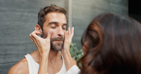 Skincare, couple and cream on face in home for skin hydration, morning routine or hyaluronic acid. Love, people or cosmetics product application for grooming, wellness support and bonding in bathroomの写真素材