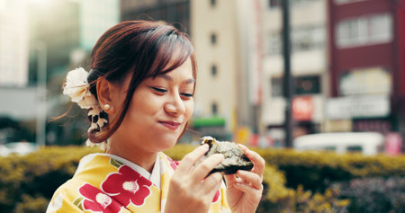 City, smile and girl in kimono eating onigiri on street with happy face, morning commute and breakfast snack. Urban, rice ball and woman with traditional Japanese clothes, food and culture for travelの写真素材