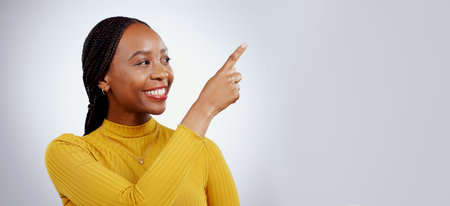 Woman, pointing and in studio announcement for discount, promotion and happy for opportunity or marketing deal. Black person, model or smile for sales choice in retail, wow news or gray backgroundの写真素材