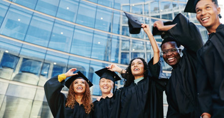 Smile, students and throw hats for graduation of learning success, class achievement and celebrate. Below, people and tradition with support, academic degree and bonding together for college ceremonyの写真素材