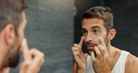 Skincare, mirror and man with face cream in bathroom for skin hydration, grooming treatment and morning routine. Hygiene, reflection and spf lotion application for moisturizer, wellness or anti agingの写真素材