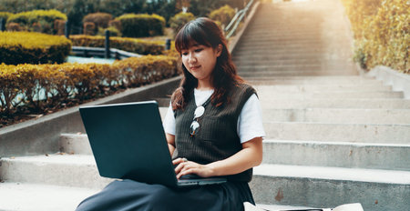 Woman, laptop and outdoor stairs for university, student studying and online for assignment. Person, campus park and college website for module learning, education and course for knowledge in Japanの写真素材