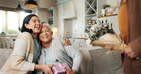 Birthday, gift or laughing with family on sofa in living room of home together for bonding or celebration. Box, funny or hugging with senior woman and daughter in apartment for event or milestoneの写真素材