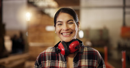 Portrait, happy carpenter and woman in workshop for furniture manufacturing and production. Woodwork, smile and professional at industrial factory for joinery, carpentry and ear protection headphonesの写真素材