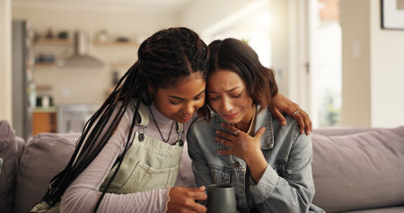 Women, friends and sad with support on sofa for comfort, understanding or sympathy at home. Female people, confession or upset with drink, breakup or empathy for friendship, soothing or care at houseの写真素材