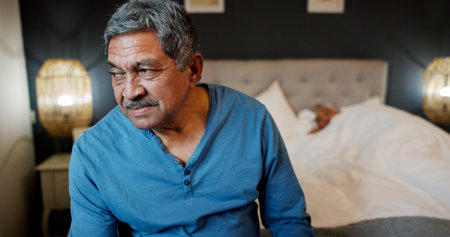 Sad, senior man and thinking on bed with insomnia, mental health and guilt for decision. Bedroom, elderly person and regret in home with remember, thoughtful and unhappy for mistake in retirementの写真素材