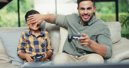 Boy, father and cover eyes with video game on sofa, controller and contest with bonding, love and playful. People, dad and child with console for challenge, competition and cheating in family houseの写真素材