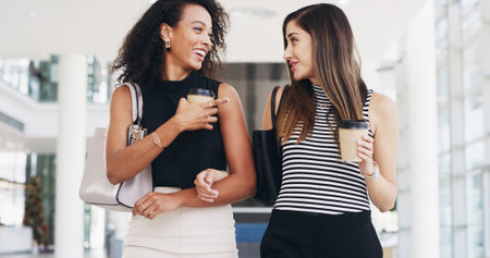 Business women, coffee and friends in office for conversation, walking and smile. Workers, team and together in lobby with drink, collaboration or laugh at funny gossip in creative startup on breakの写真素材