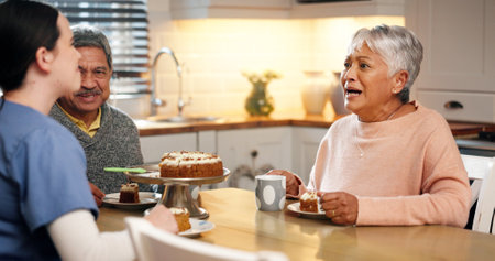 Cake, conversation and nurse with senior people for birthday, good news or celebration of treatment success. Dessert, helping and caregiver with elderly couple for party at assisted living home.の写真素材