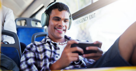 Happy man, phone or playing with headphones on bus for travel, local commute or entertainment. Male person, traveler or mobile gamer with smile for online streaming app or network in public transportの写真素材