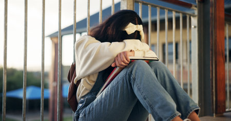 Girl, sad and lonely with crying at school with depression, bullying or social isolation on ground. Child, teenager and anxiety with books, mental health and education with scholarship at academyの写真素材
