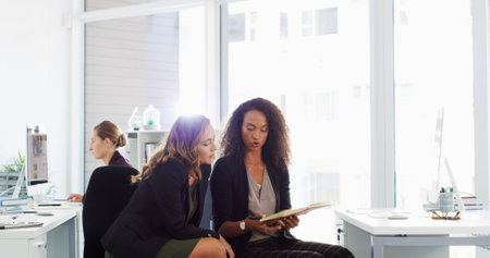 Office, discussion and business women with notebook for planning, collaboration and feedback for project. Professional, corporate and people in meeting with notes for research, proposal and websiteの写真素材