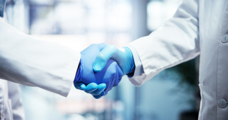 People, scientist or gloves with handshake for partnership, medical agreement or deal at hospital. Closeup, teamwork or health employees shaking hands with meeting for research, b2b or clinic trialの写真素材