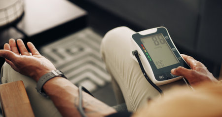 Home, blood pressure and hands of man with machine for test, hypertension and check pulse on sofa. Healthcare, above and person with medical equipment for exam, monitor and measure heart rateの写真素材