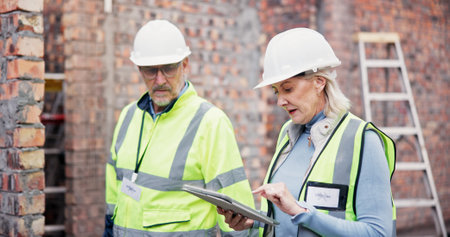 Construction, online and colleagues with tablet, outdoor and discussion for project management and team. Architecture, mature woman and man with tech for digital blueprint, collaboration and talkingの写真素材