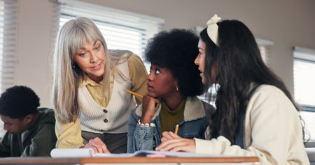 School, college and teacher with students help for assessment, assignment and explain test question. University, academy and educator with girls for learning, teaching and education in classroomの写真素材