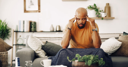 Home, tired and man with headache, stress and burnout with pain in living room. Person, apartment and guy on sofa with migraine, fatigue and exhausted with strain and pressure on temple from overworkの写真素材