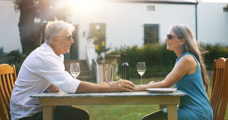 Love, holding hands and wine with old couple in nature for romance, anniversary date and bonding. Happiness, retirement and support with senior man and woman at resort for glass, relax and vacationの写真素材