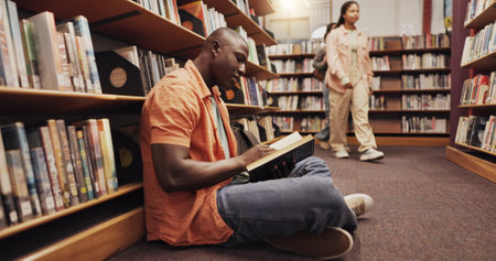 Student, black man and reading on floor in library for literature, research and studying of knowledge. Person, novel and search for academic information, school book and learning for education growthの写真素材