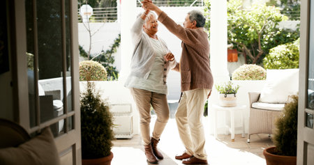 Mature couple, dancing and spin in home with love, bonding and celebration for anniversary. People, man and woman with holding hands, retirement and smile for twirl, rhythm and relationship at houseの写真素材