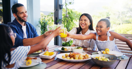 Happy family, lunch and cheers with juice for celebration at outdoor patio with love, care and bonding together. Mom, dad and kids toast with drink glass for food or healthy meal with parents at homeの写真素材