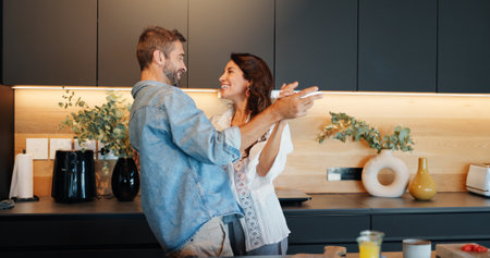Mature couple, smile and dancing in kitchen with love, bonding and celebration for anniversary in home. People, man and woman with holding hands, excited or playful rhythm for relationship at houseの写真素材