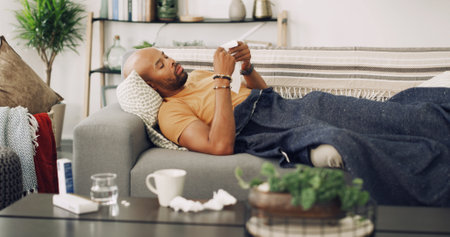 Living room, sick and man with tissue, sofa and allergies for sinus, season and sneezing with infection. Couch, blanket and symptoms with fever, runny nose and health of person with virus in houseの写真素材