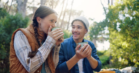 Outdoor, camping and couple with coffee, drinking and bonding with warm beverage in nature and adventure. Hiking, travel and people with hot tea for cold weather, traveller and tourists on vacationの写真素材