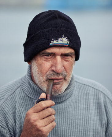 Fisherman portrait, mature and man with smoking pipe by nature at a port for fishing. Old man face, elderly and senior dock worker sitting outdoor with tobacco smoke product at a harbor for workの写真素材