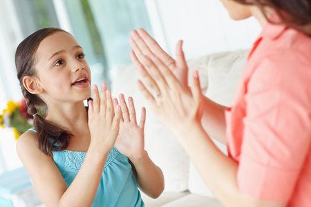 Mother, child and clapping on sofa for game, cooperation and communication for skills development. Home, mom and girl with playful for bonding, dexterity and coordination with hands in living roomの写真素材