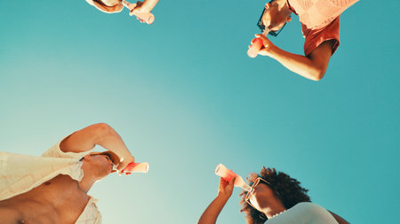 People, drinks and sky with friends, low angle and outdoor on vacation, break and event in summer. Men, women and bottle for soda with party, solidarity and nature with social group on holidayの写真素材